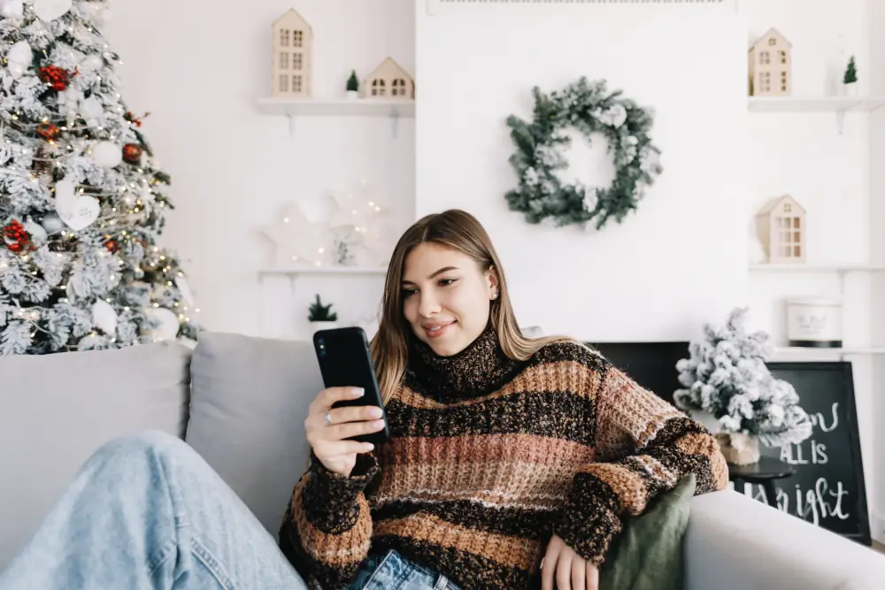 Heat Pump Efficiency During The Holidays: Stay Warm and Cozy - Young woman relaxing on the couch. Looking at her home. Holiday decorations around her.