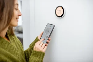 Furnace history - Woman regulating heating temperature with phone and thermostat at home