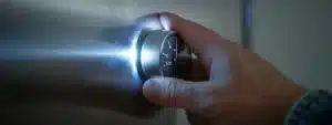 a close-up photograph of a shiny silver thermostat being checked by a homeowner's hand.